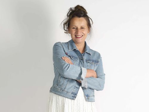 Portrait von Christine Hartge mit Jeansjacke und verschränkten Armen, sie lächelt